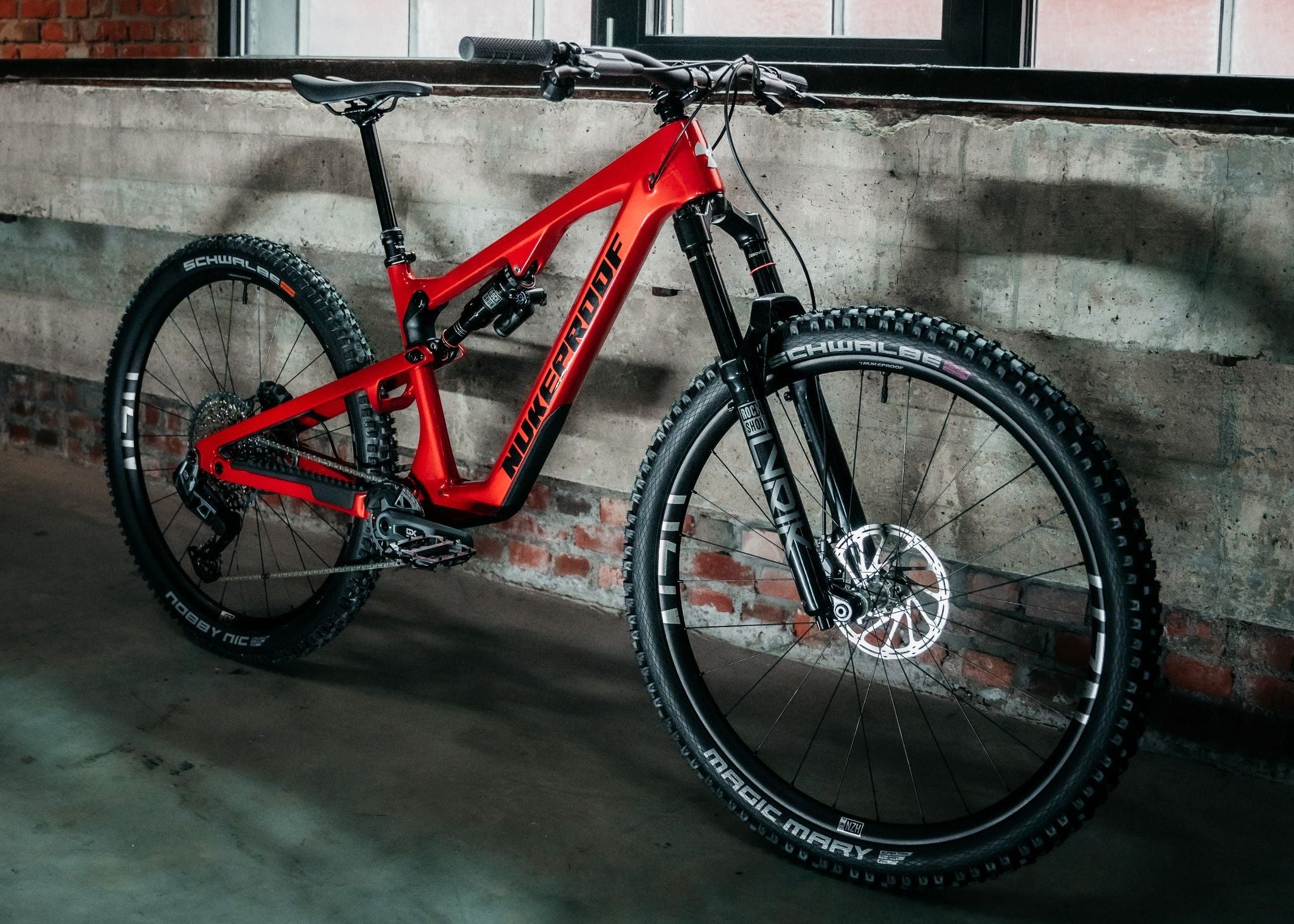 Red mountain bike leaning against a concrete wall with large windows in the background.