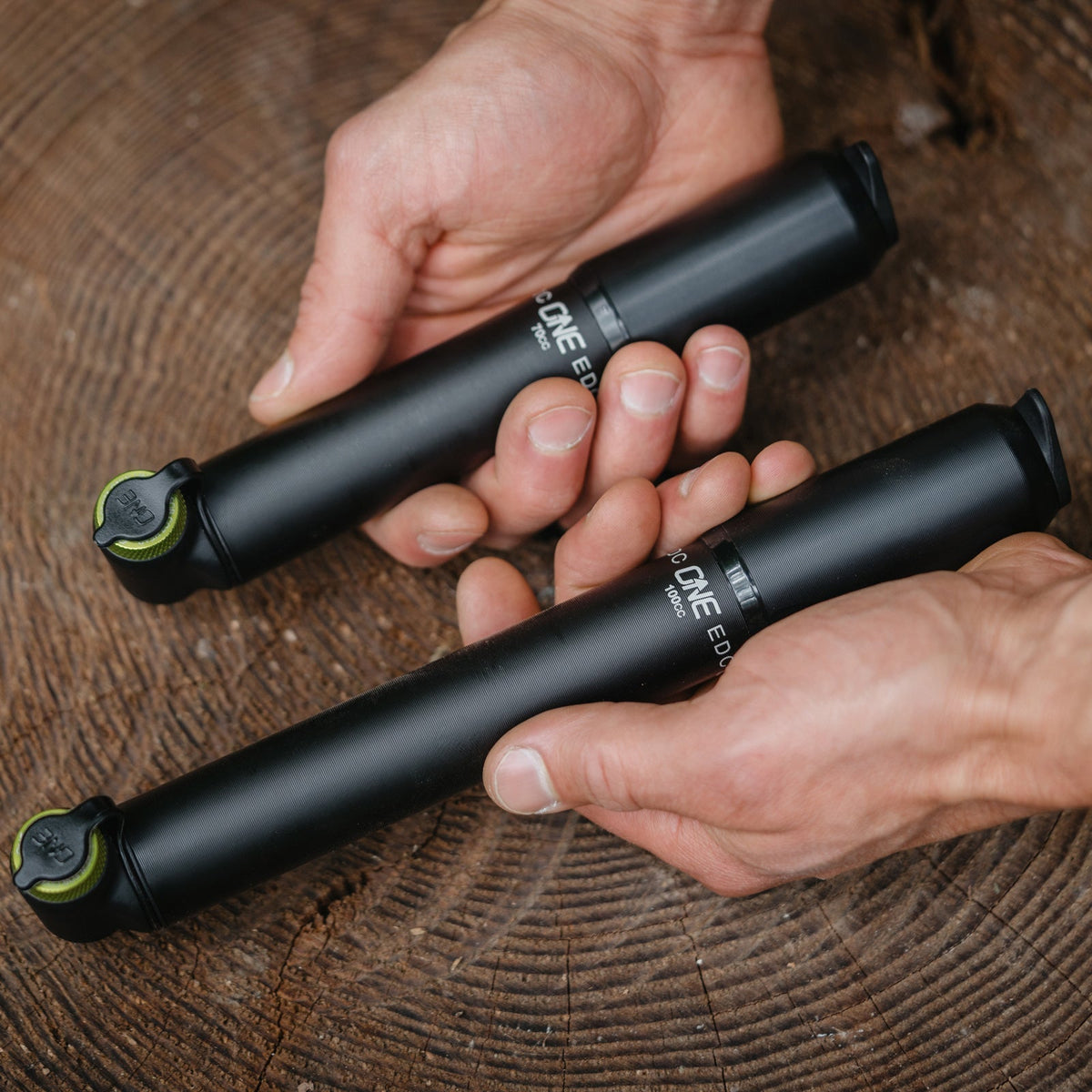 Hands comparing the 70cc and 100cc OneUp EDC Pumps