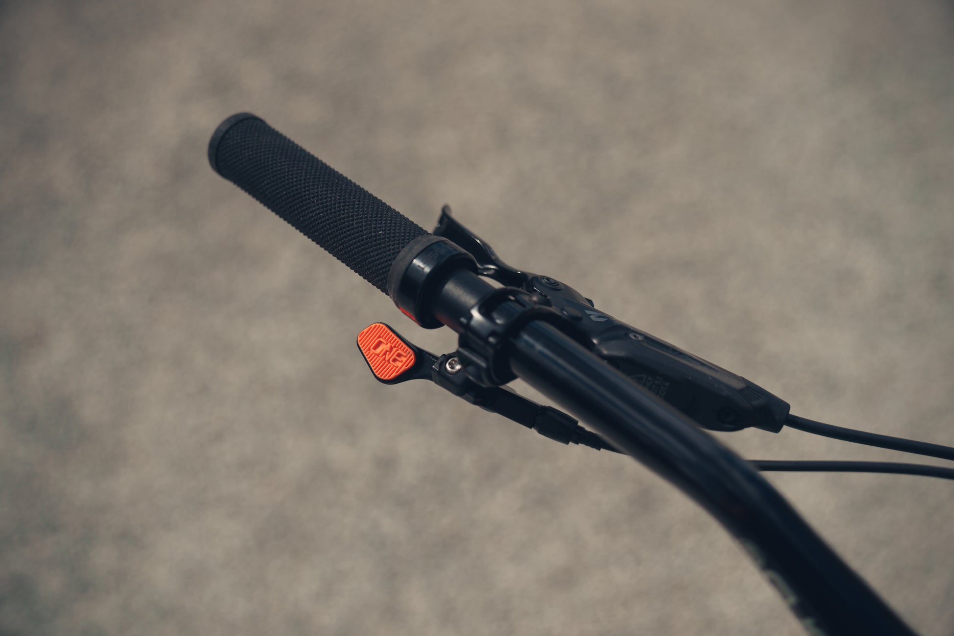 Close-up of a bicycle handlebar with a black grip and orange reflector on a blurred background