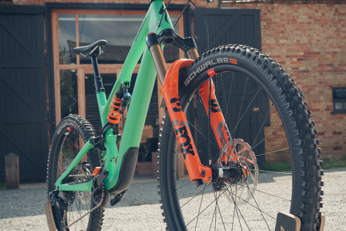 Green and orange mountain bike with Schwalbe tires against a brick building.