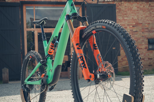 Green and orange mountain bike with Schwalbe tires against a brick building.