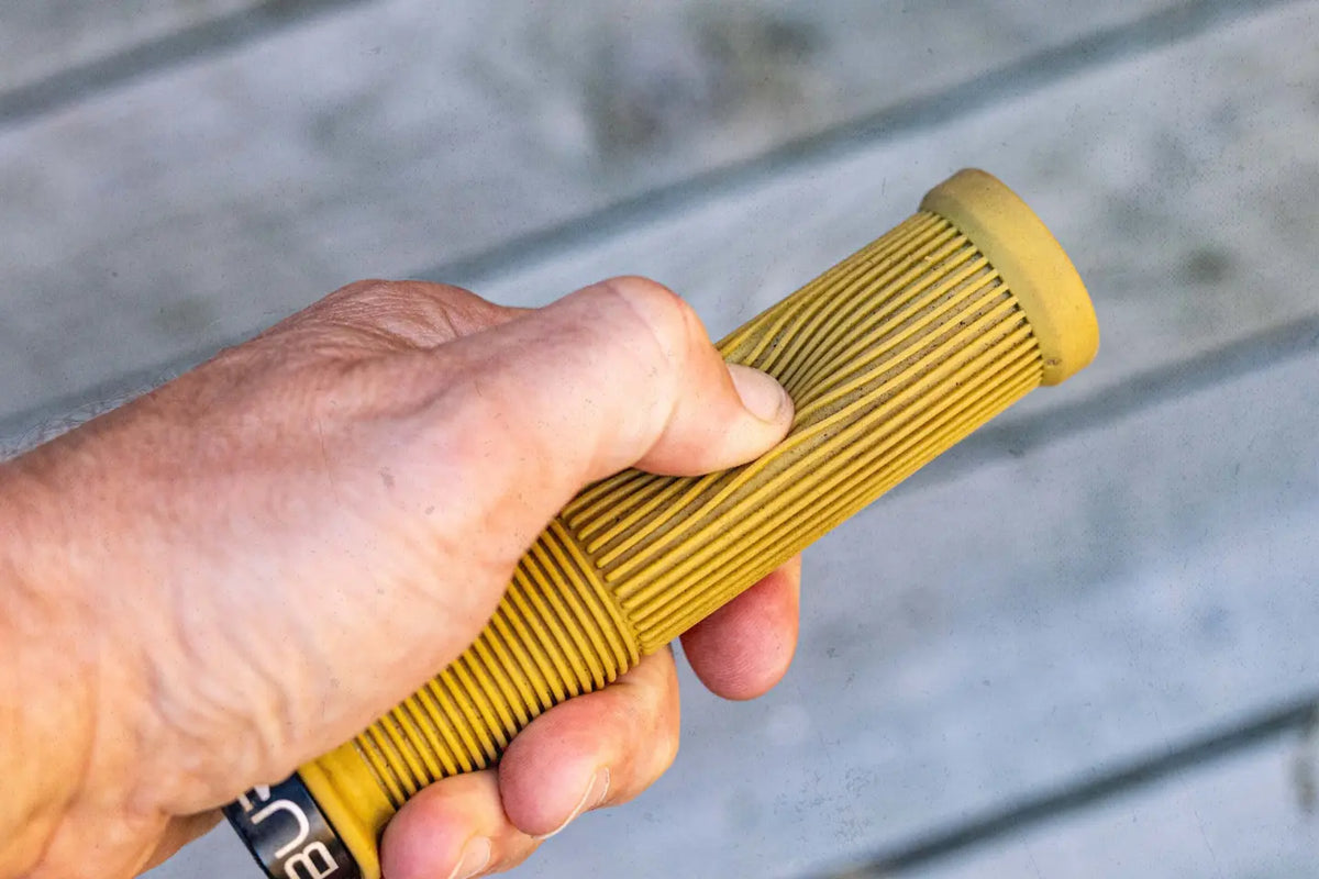 A hand compressing the ribbed rubber on a yellow Burgtec Josh Bryceland grip