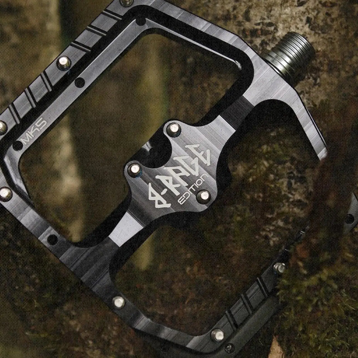 Black Burgtec B-Rage pedal resting on a log with its platform and pin layout visible