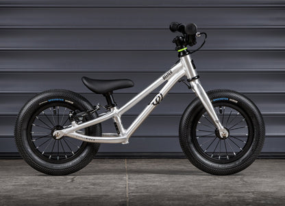 Early Rider Belter 12 Balance Bike in Brushed Aluminium - brushed balance bike profile against shutters with low frame
