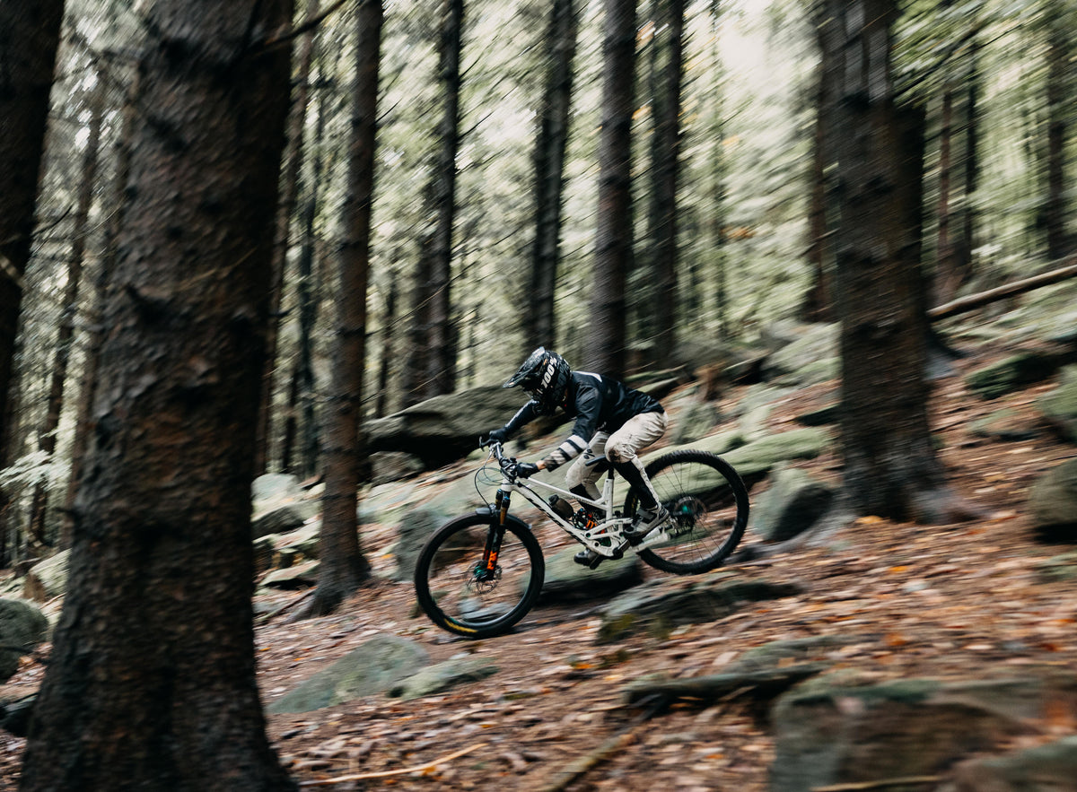 Mountain biker descending a rocky forest trail in Trickstuff Direttissima campaign imagery.