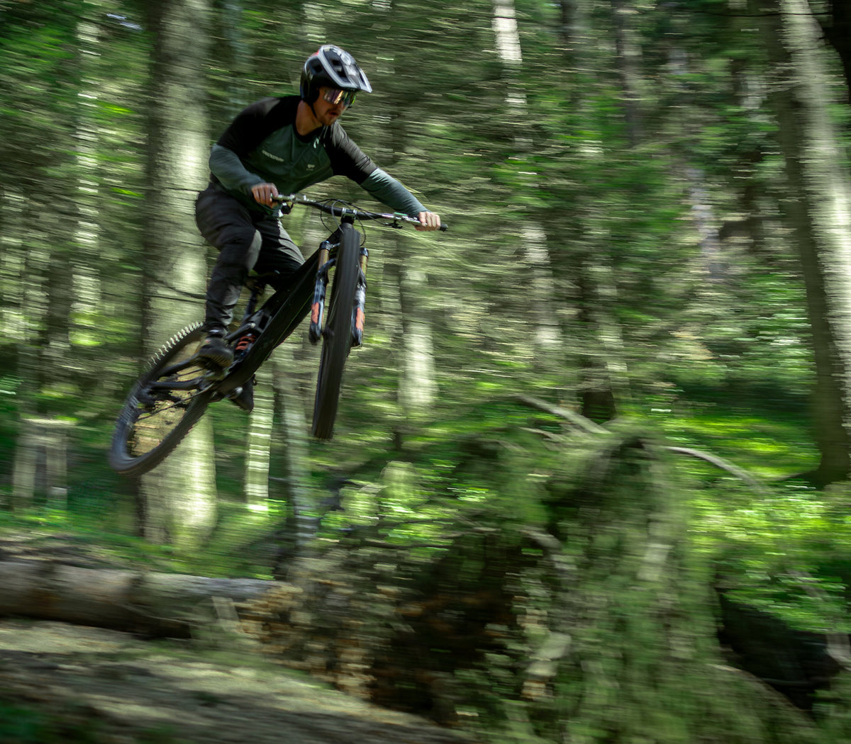Mountain biker jumping through green woodland.