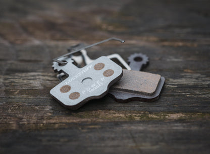 Trickstuff POWER ALU 830 brake pads and spring on wood, showing the backing and friction faces.